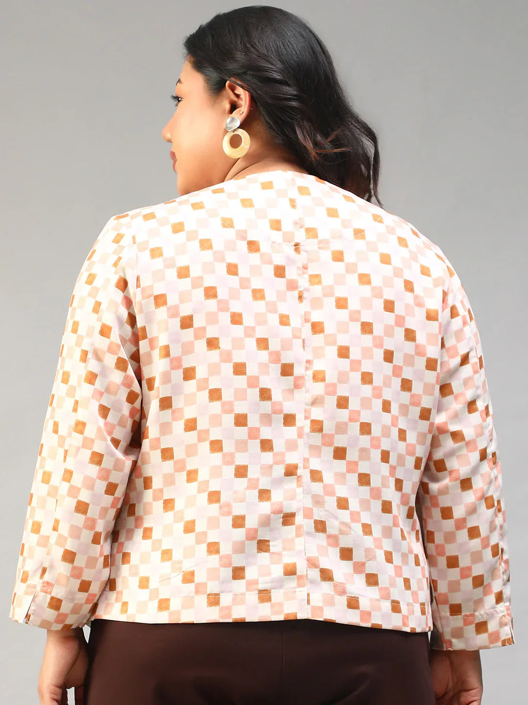 A smiling woman with long dark hair wearing a white and orange checkered jacket with buttons.