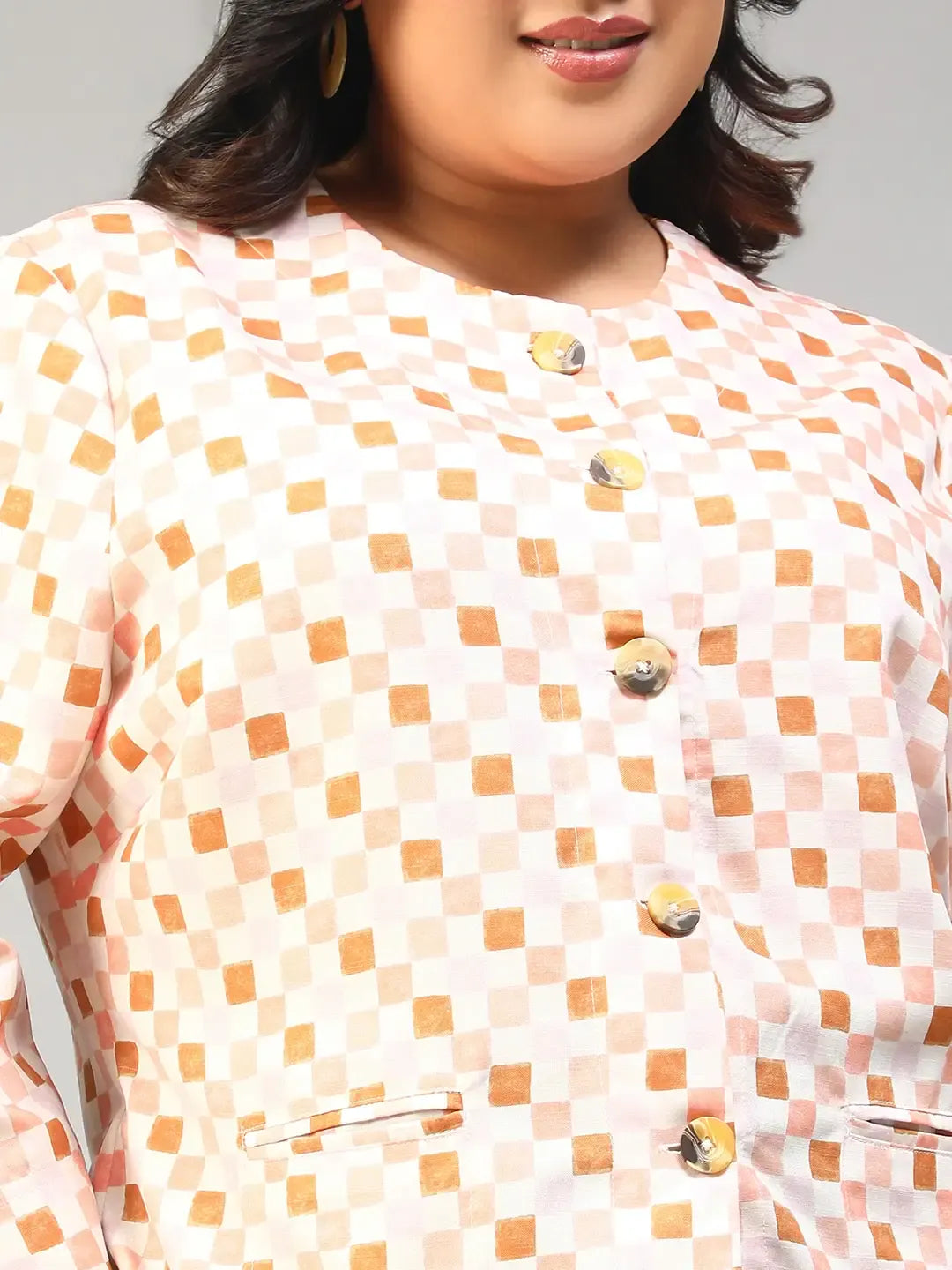 A smiling woman with long dark hair wearing a white and orange checkered jacket with buttons.
