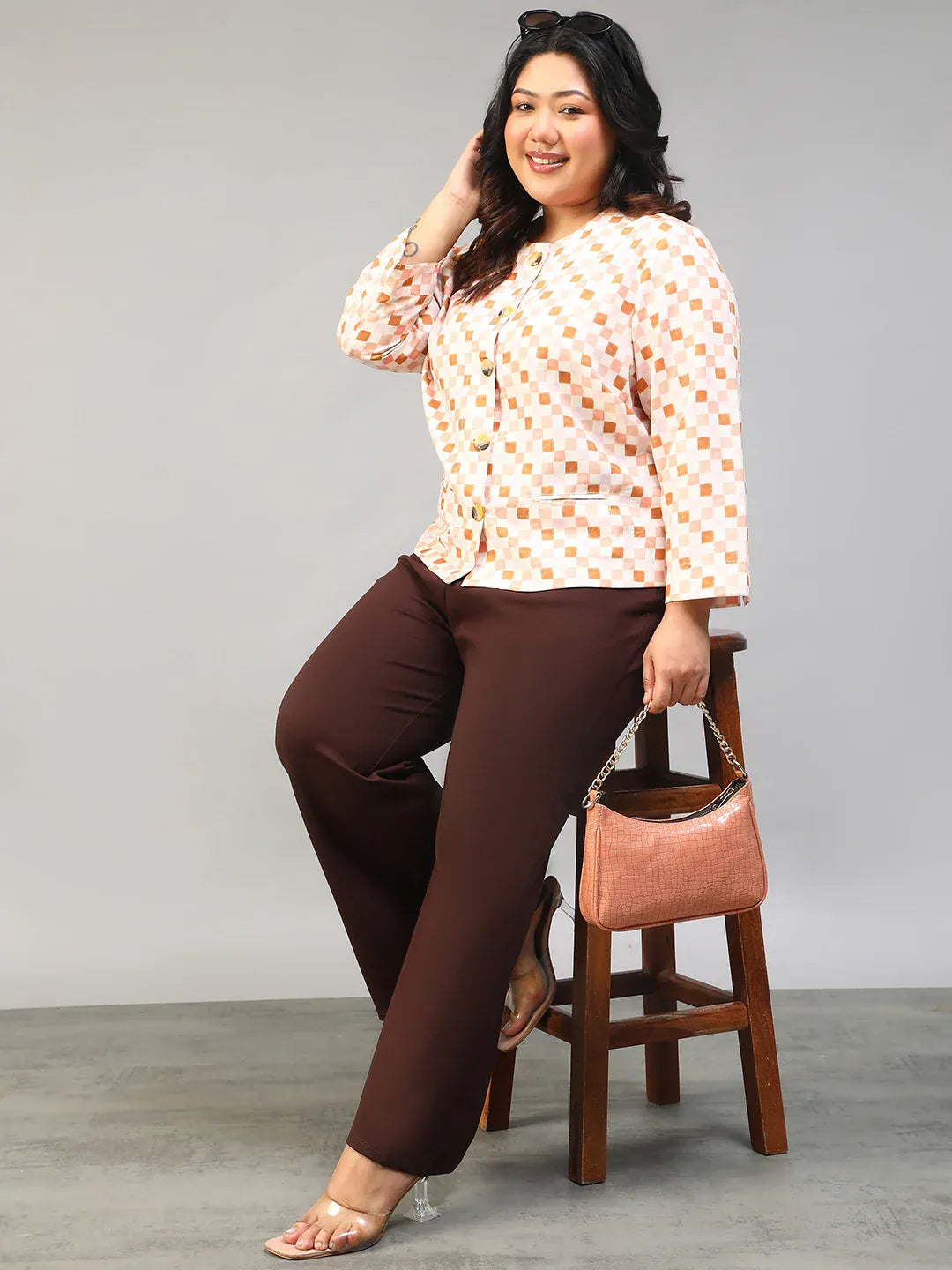 A smiling woman with long dark hair wearing a white and orange checkered jacket with buttons.