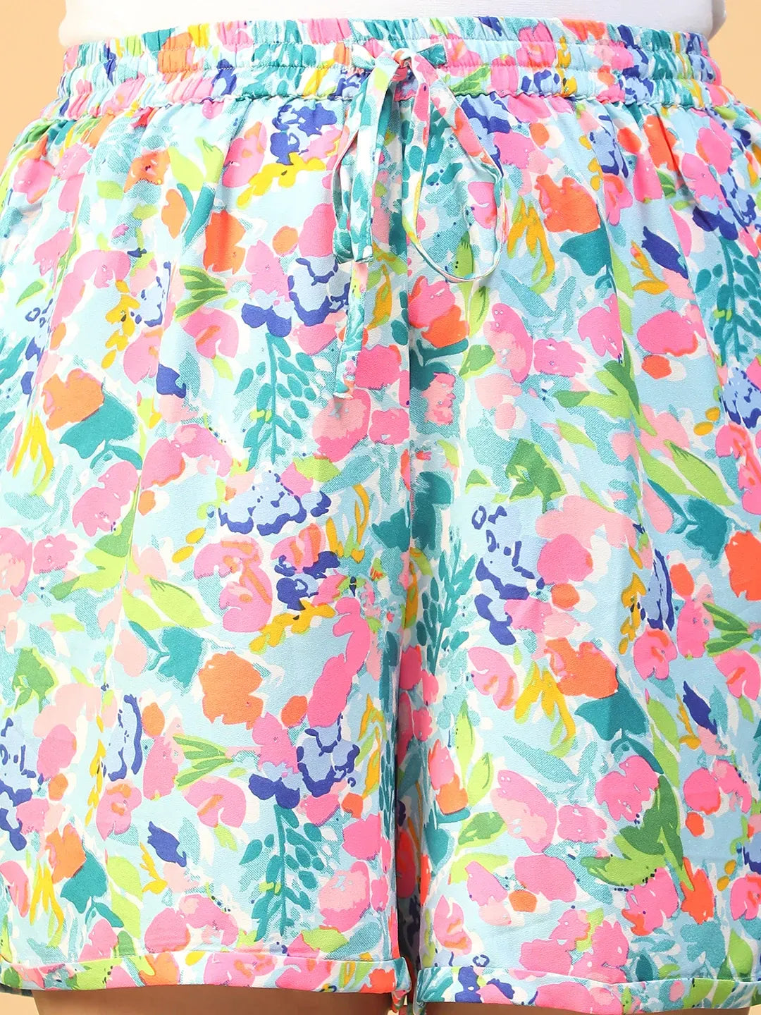 A person wearing colorful floral shorts and white sneakers stands against a white background.