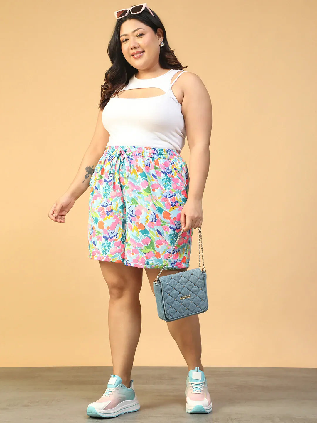 A person wearing colorful floral shorts and white sneakers stands against a white background.
