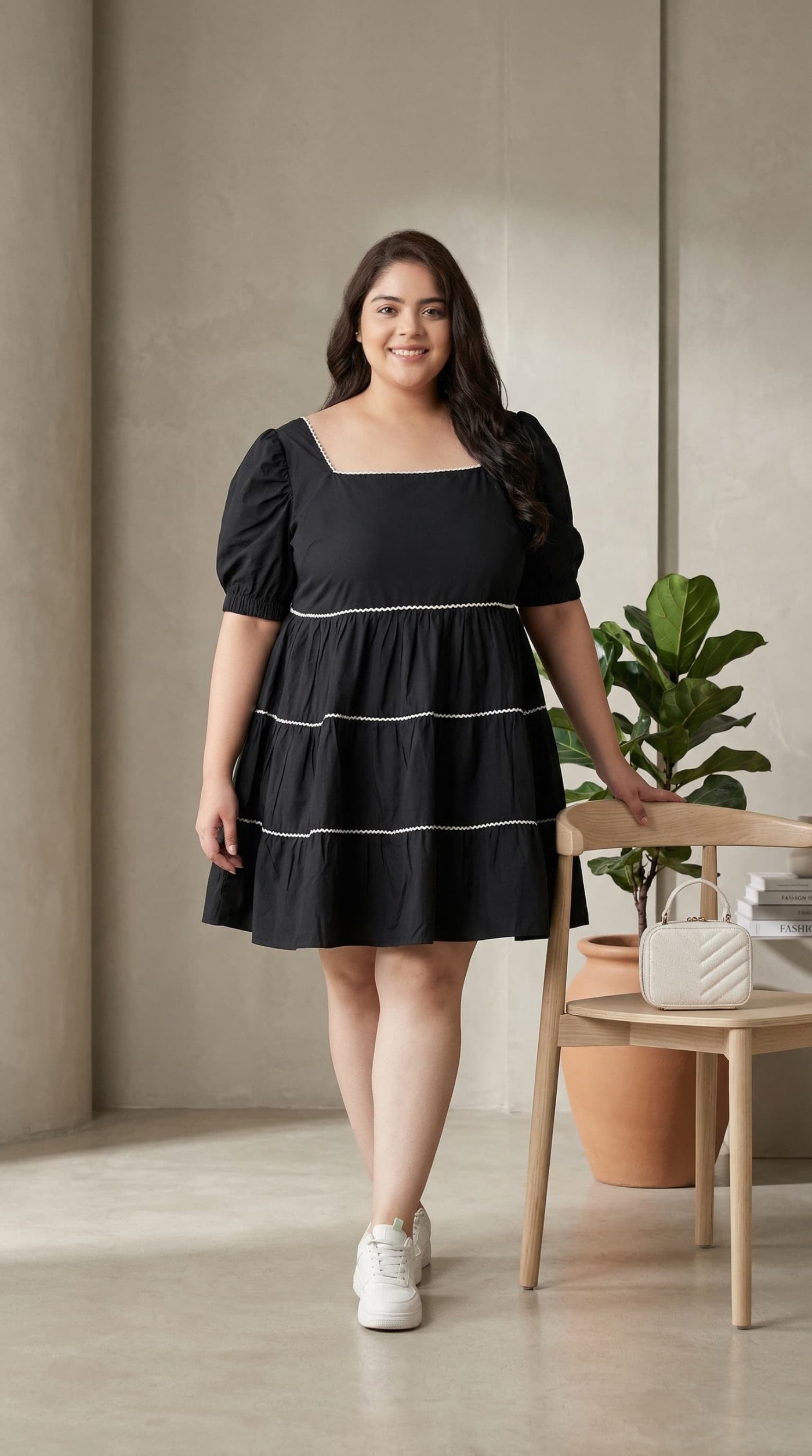 Woman wearing a black dress standing in a room with a plant and table.