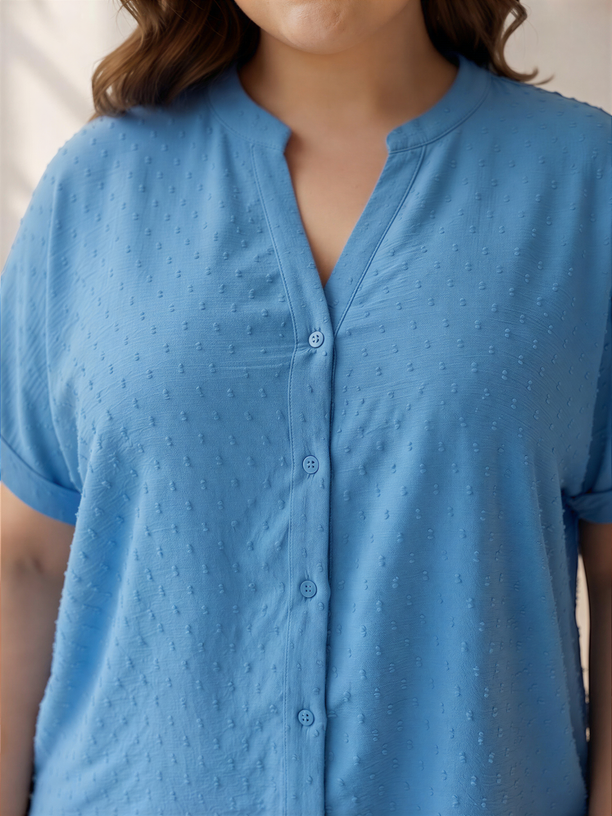 A close-up image of a woman wearing a blue shirt with a v-neck and short sleeves.