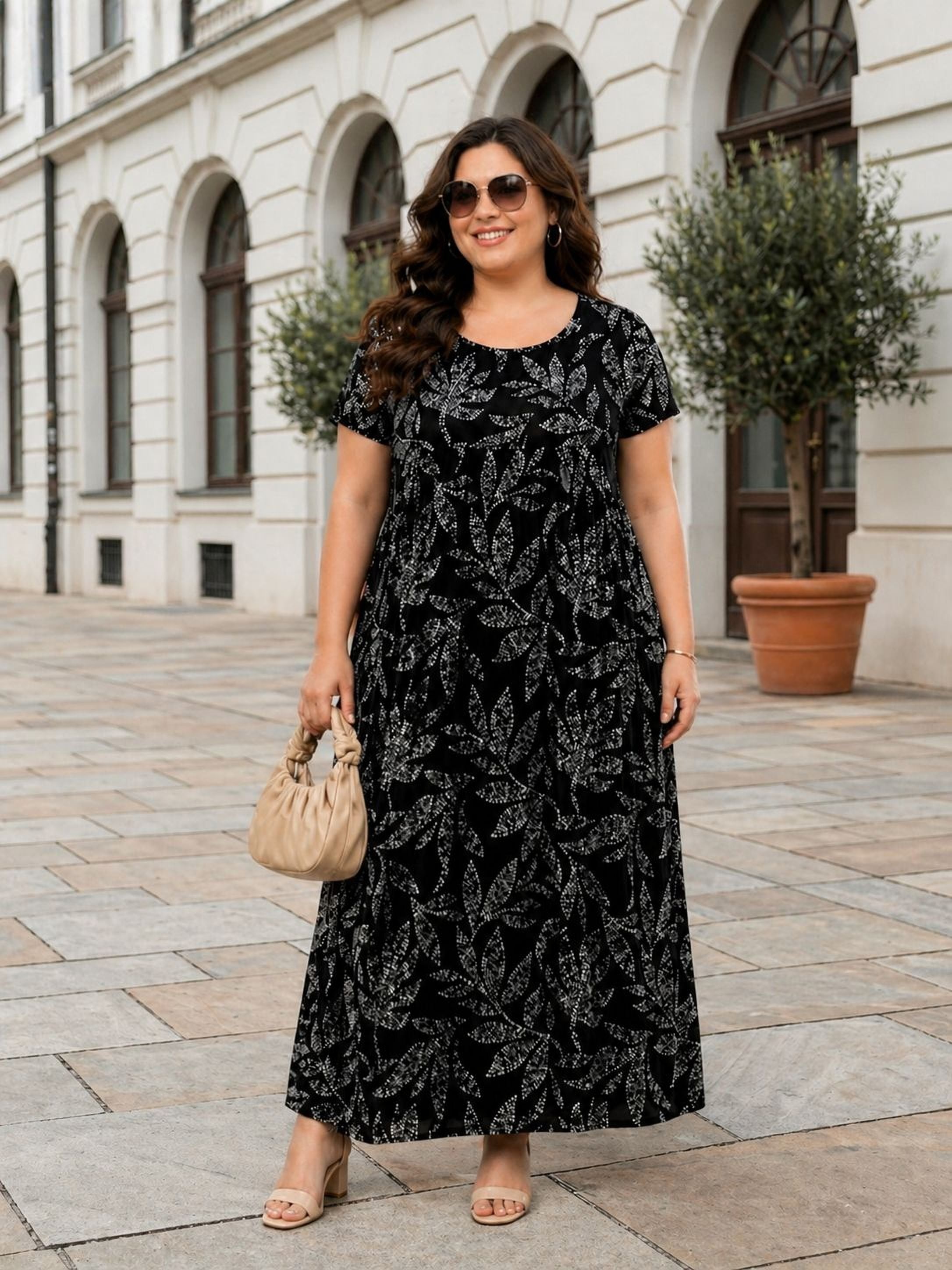 A woman wearing a black and white floral print dress and sunglasses stands on a sidewalk in front of a building.