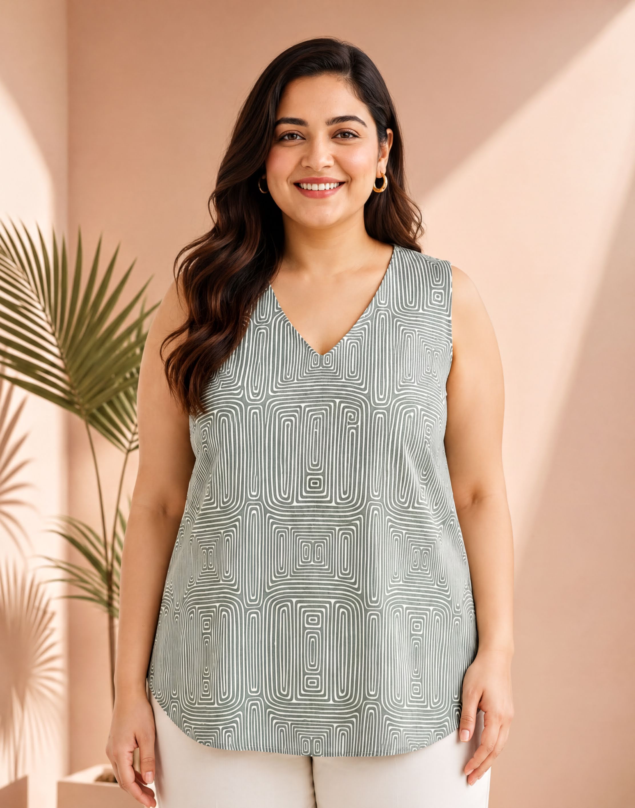 A woman with long dark hair is smiling and wearing a sleeveless top with a patterned design.