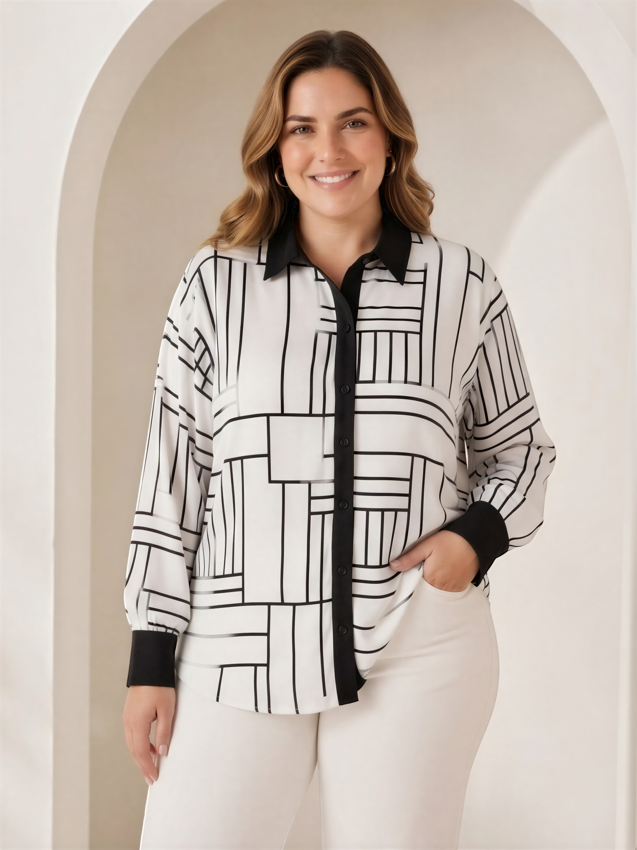A woman wearing a white and black patterned blouse with a black collar and sleeves, standing in front of a white archway.