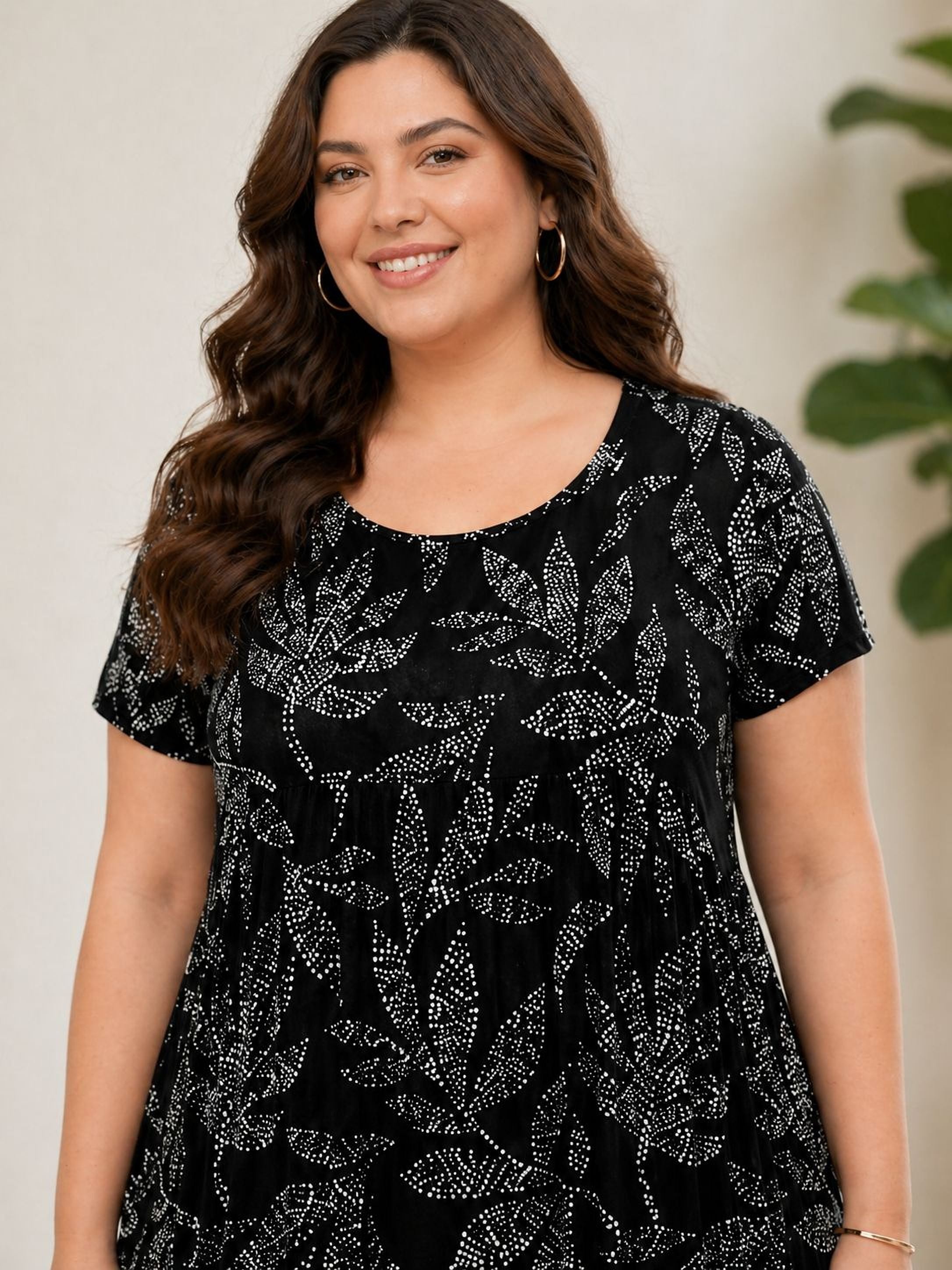 A woman with long brown hair is smiling and wearing a black dress with a leaf pattern.