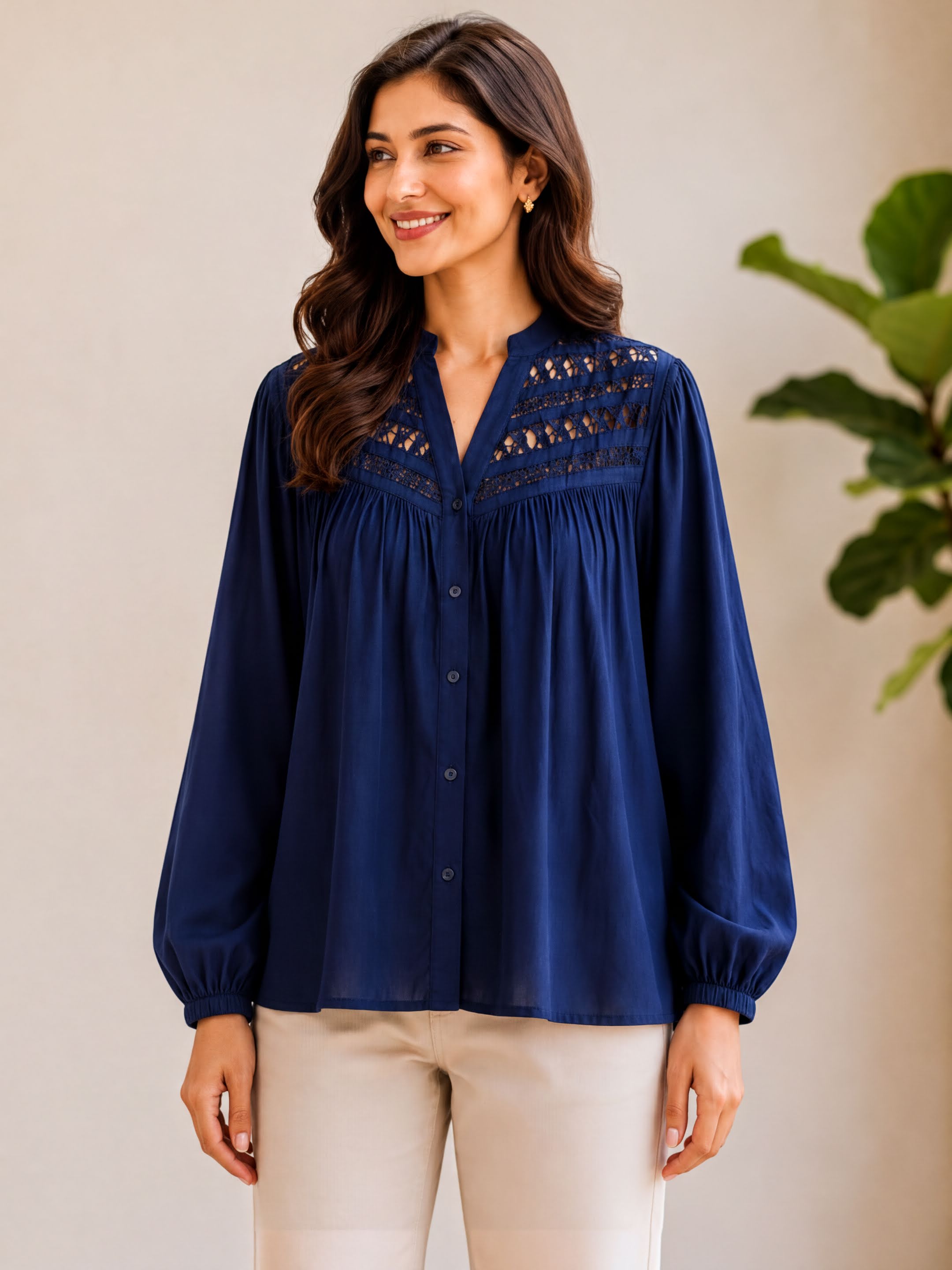 A woman with long brown hair is smiling and wearing a navy blue blouse with a v neck and puffed sleeves.