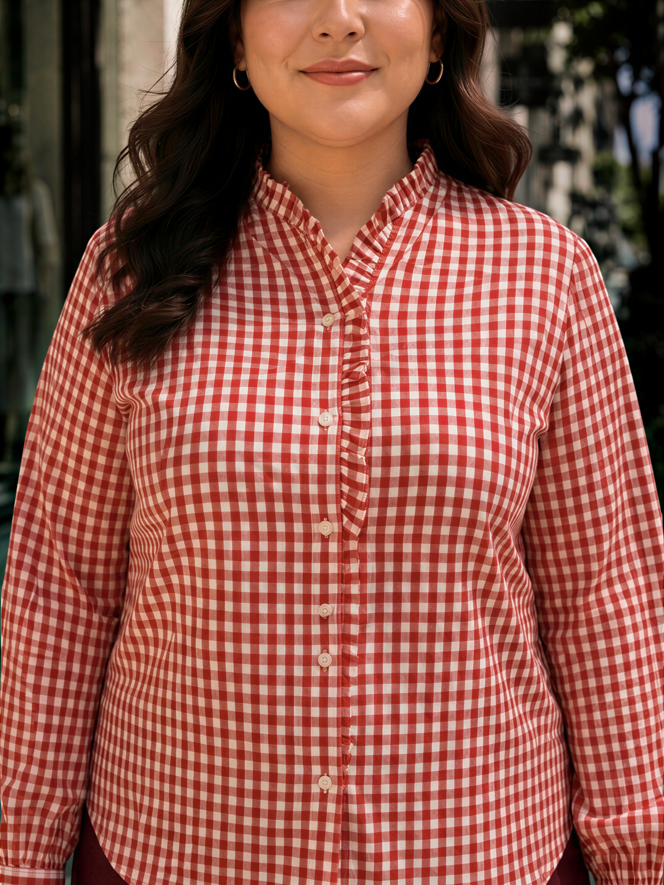 A woman wearing a red and white checkered shirt with a collar and buttons, smiling at the camera.