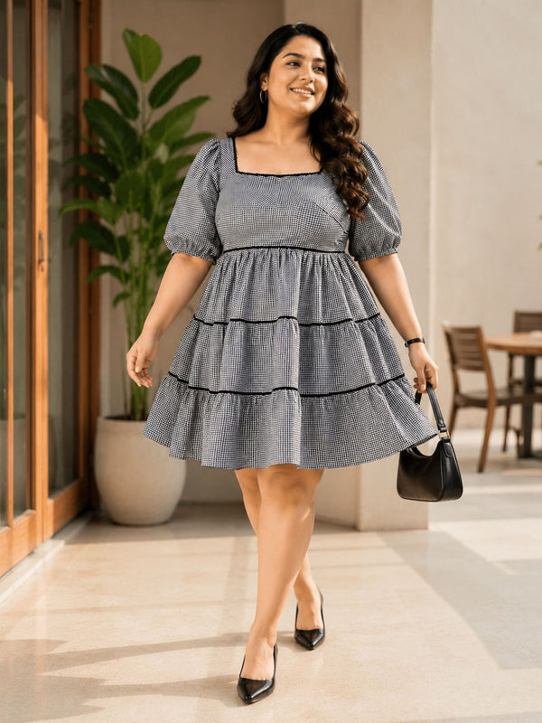A woman wearing a gray and black striped dress with puffed sleeves and a ruffled skirt, smiling and walking in a room with a potted plant and wooden furniture.