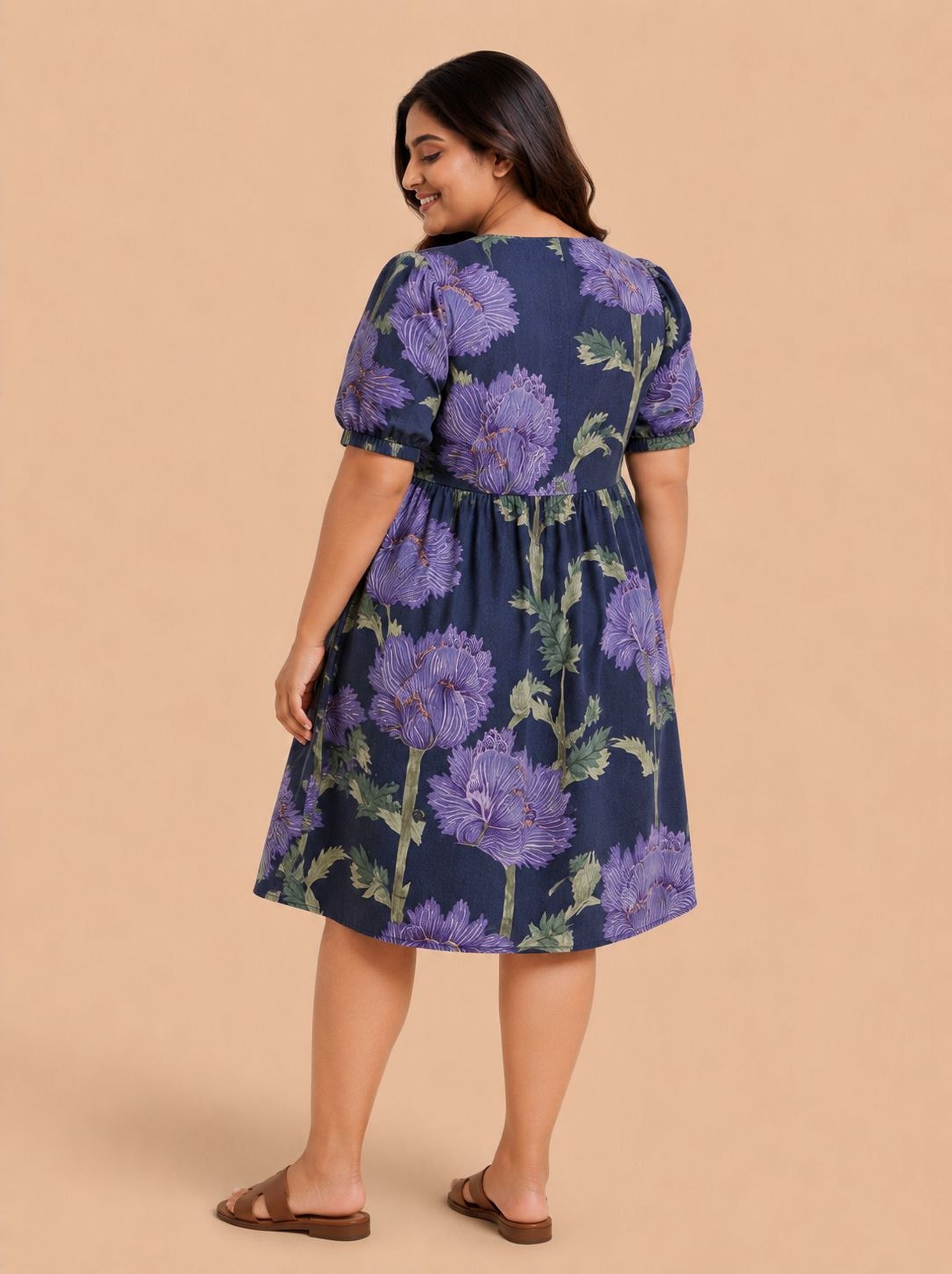 A woman wearing a blue dress with purple flowers, smiling and looking away from the camera.