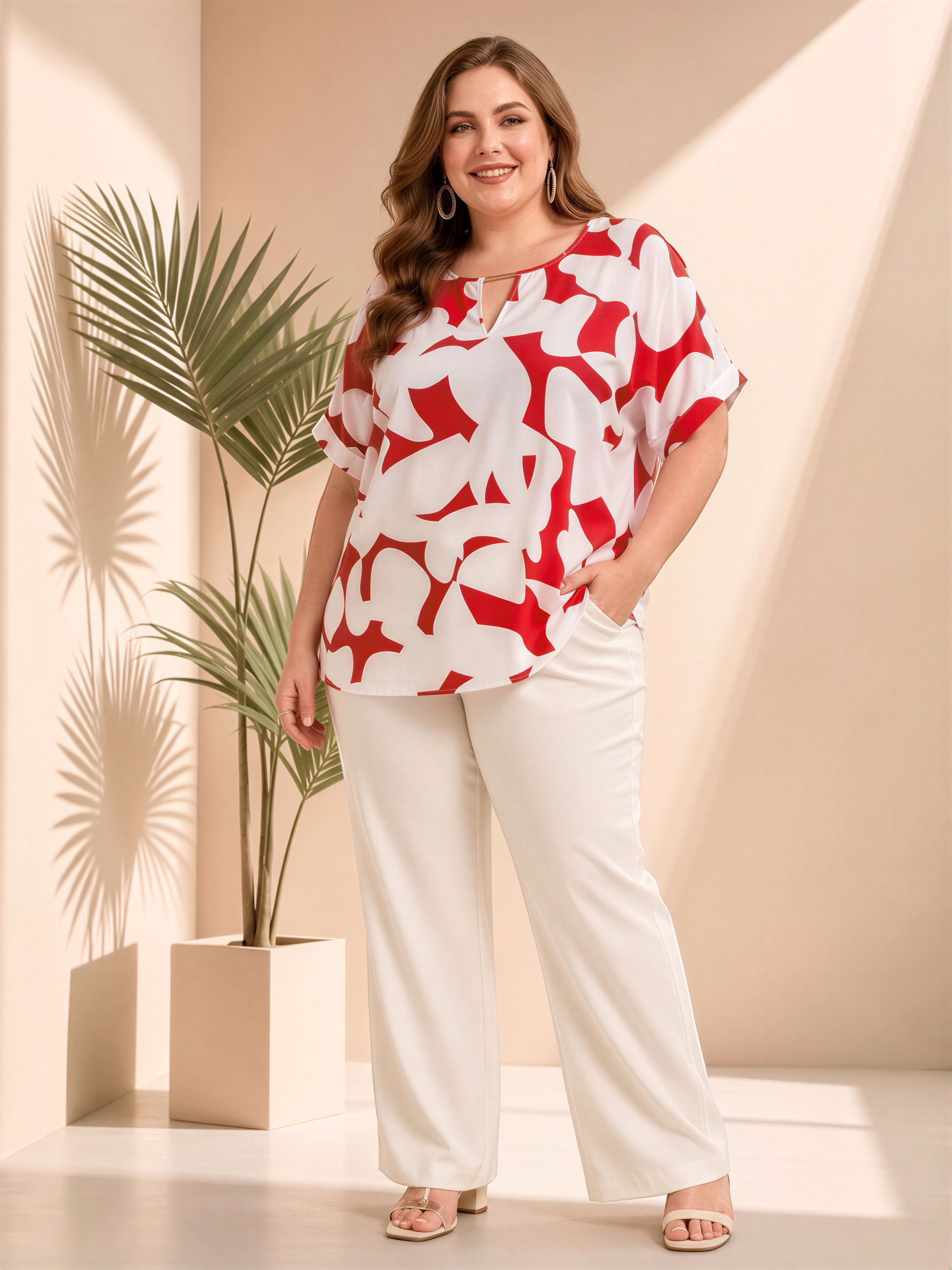 A woman wearing a red and white patterned blouse and white pants stands in a room with a potted plant in the background.