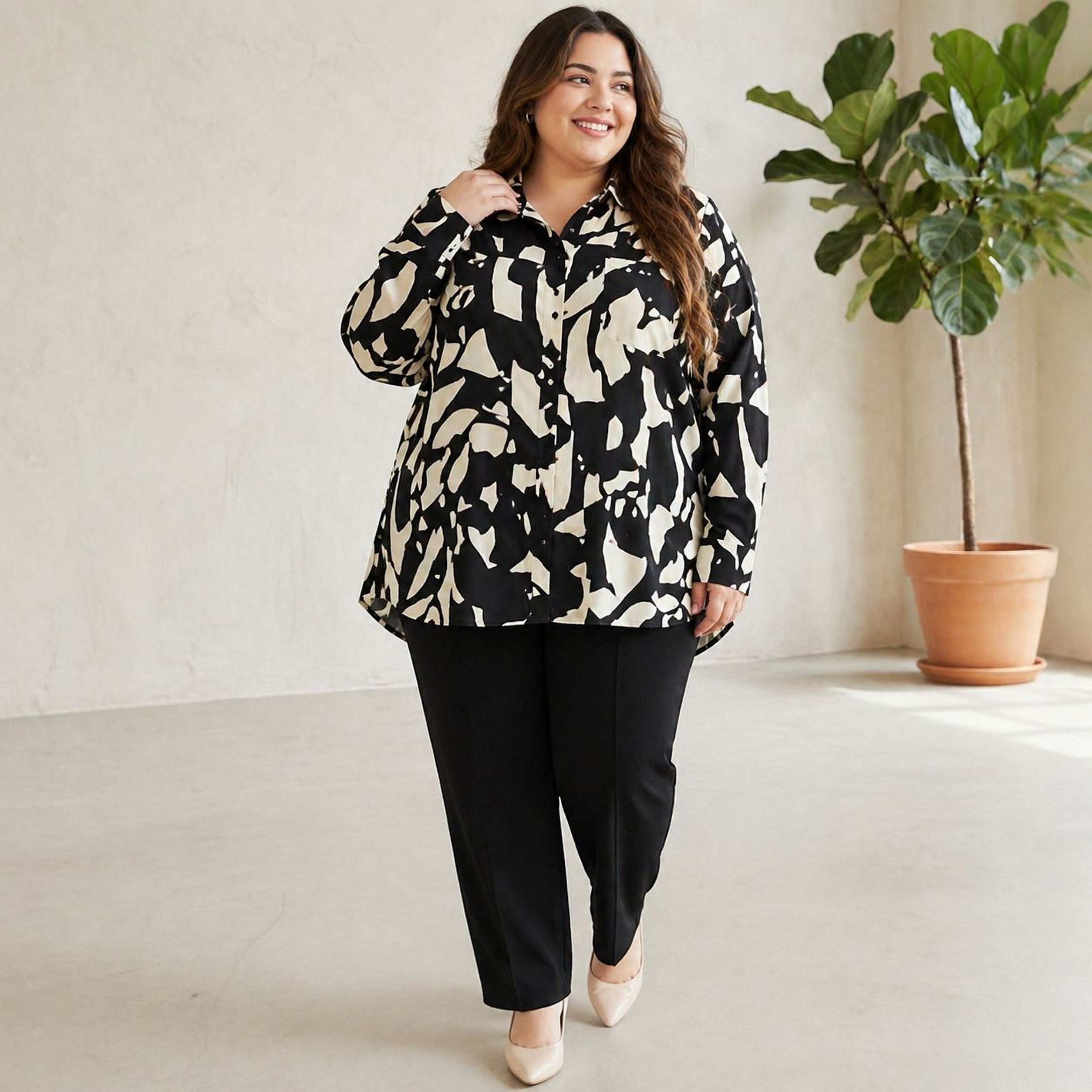 A woman wearing a black and white patterned blouse and black pants is standing in a room with a potted plant in the background.