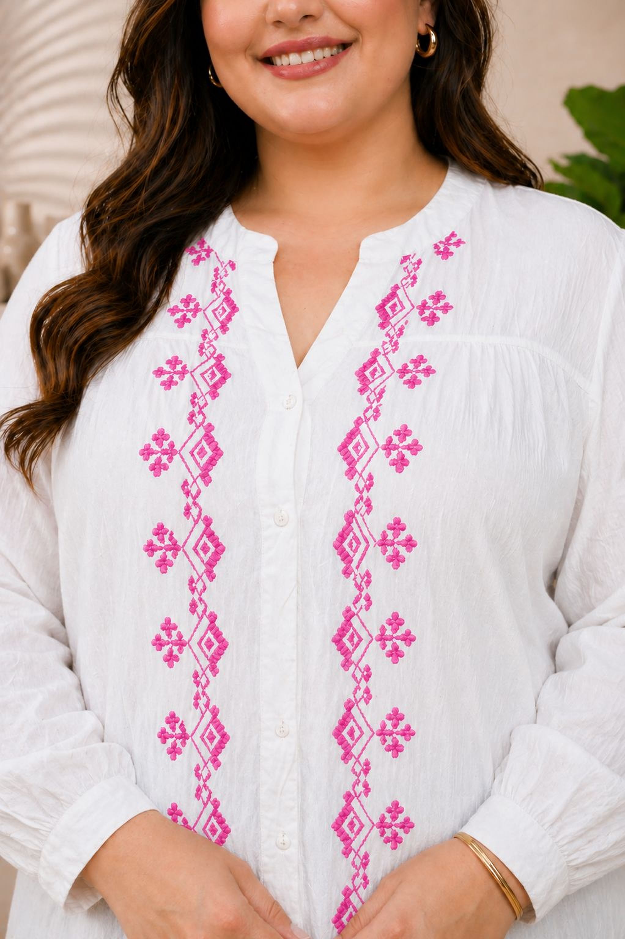 A woman wearing a white blouse with pink embroidered designs on the sleeves and collar.