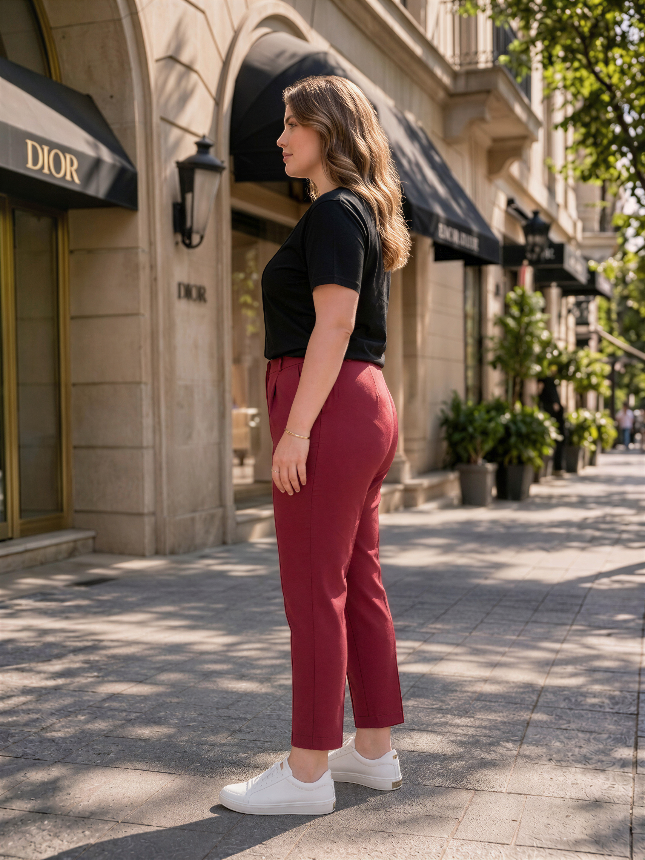 A woman in a black top and red pants stands on a sidewalk in front of a building with a Dior store sign.