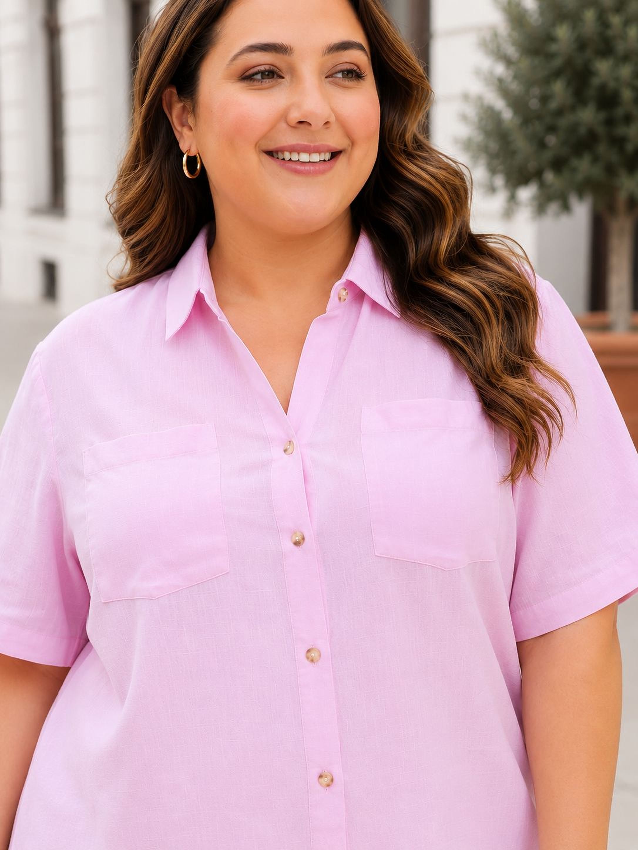 A woman with long brown hair is smiling and wearing a pink button-up shirt.