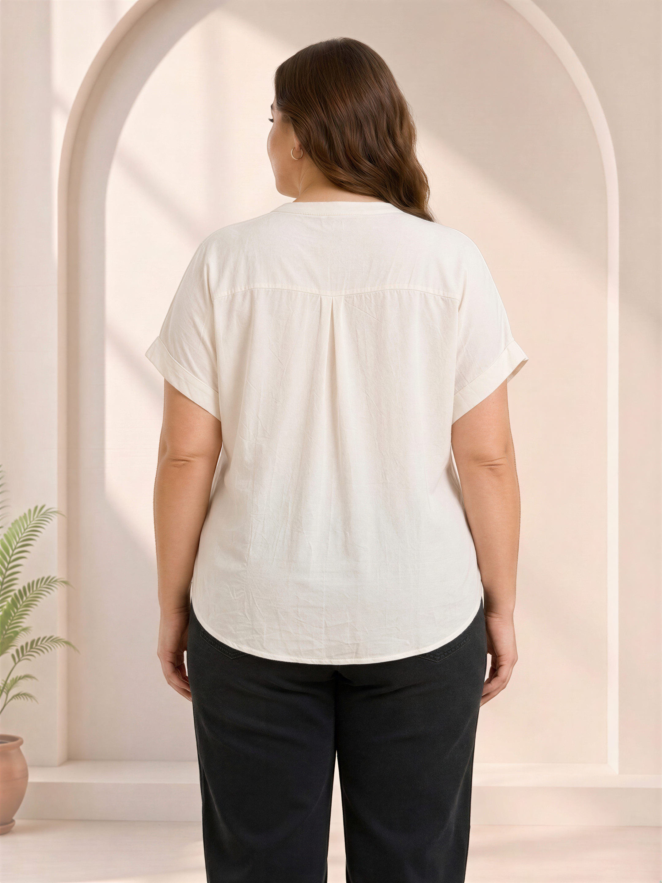 the back view of a woman wearing a white blouse and black pants, standing in front of a white archway.