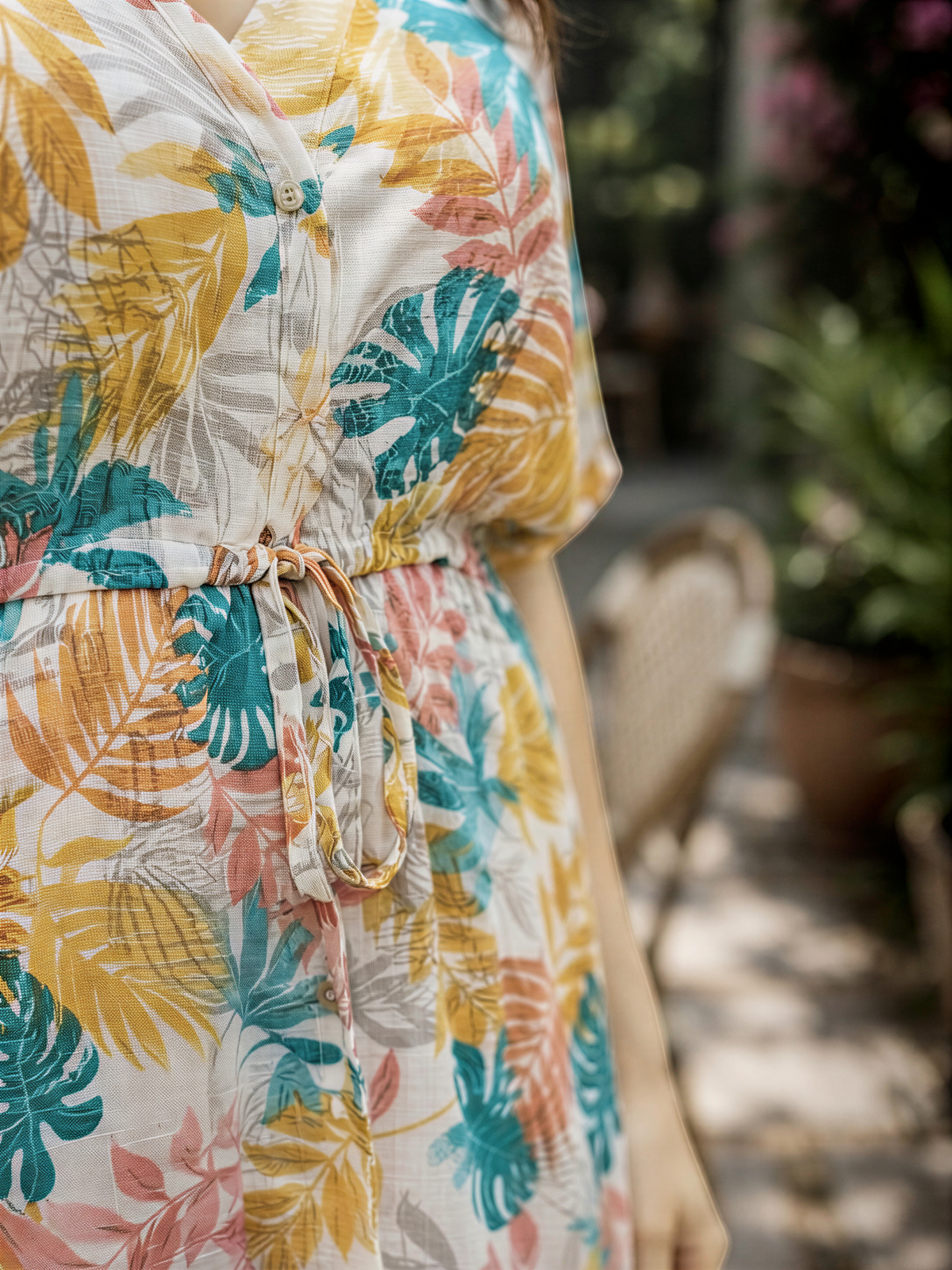 A colorful floral print dress with a tie waist, featuring a mix of yellow, green, and orange tropical leaves.
