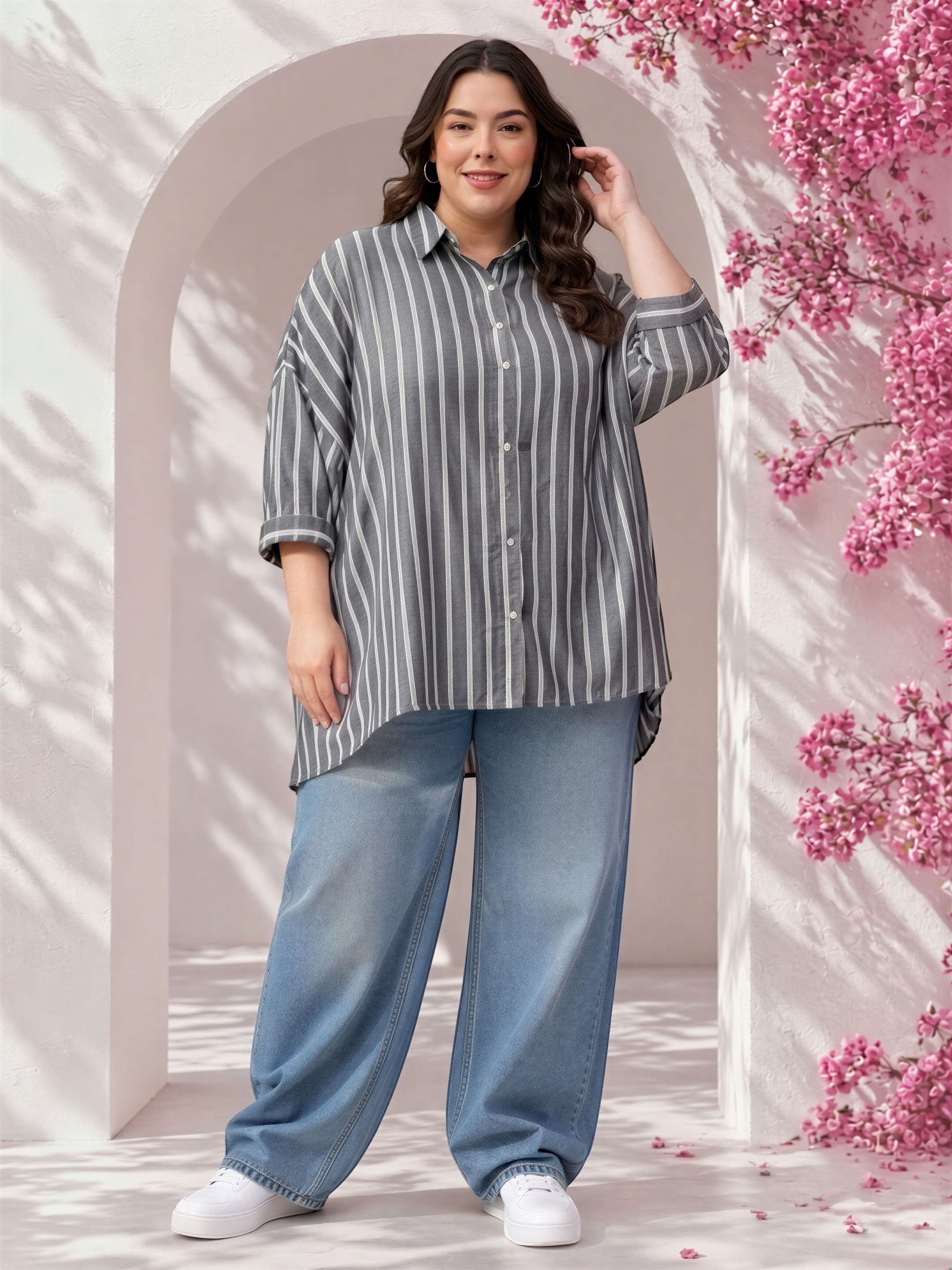 A woman wearing a striped shirt and jeans stands in front of a pink floral backdrop.