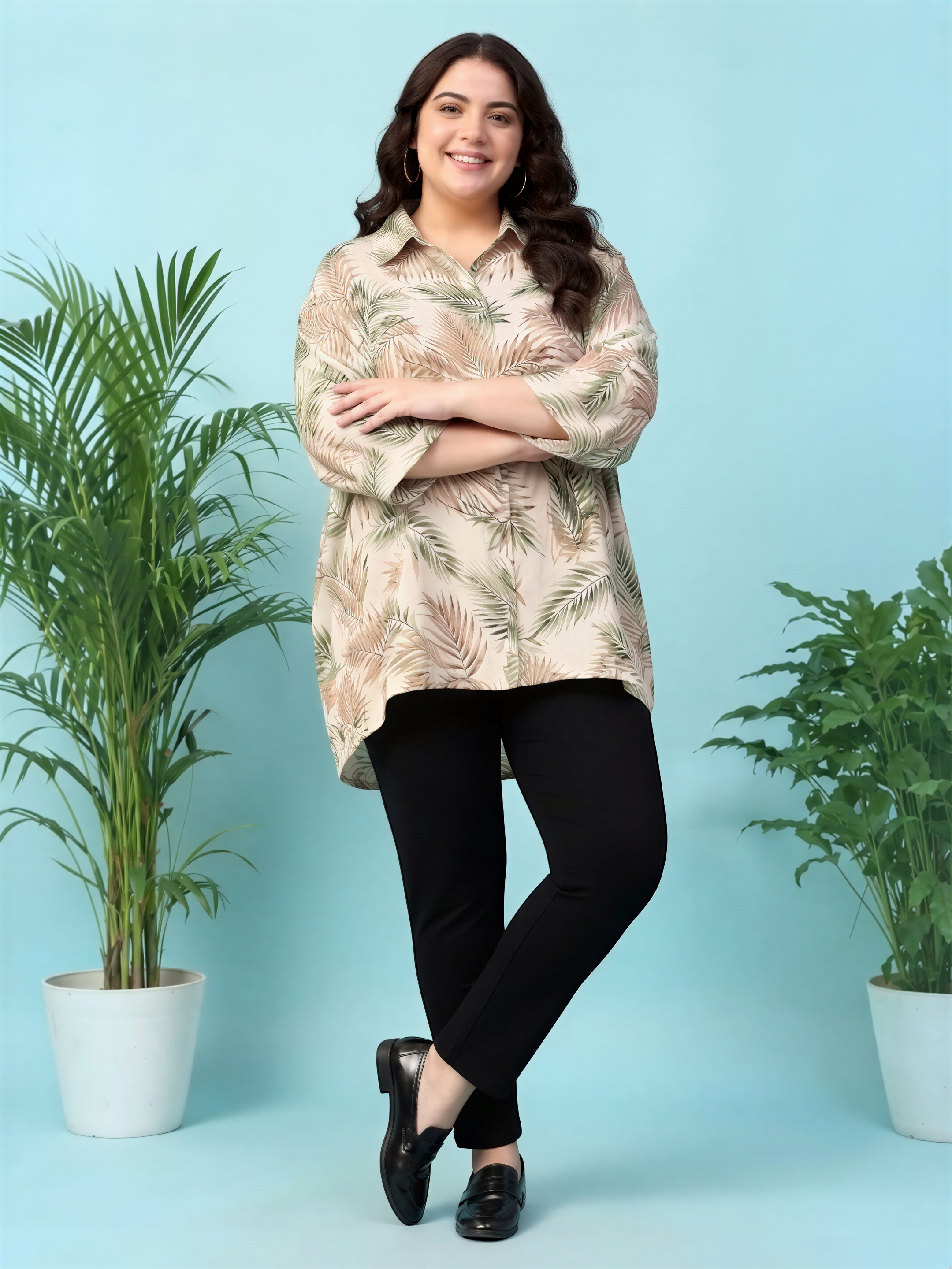 A woman with long brown hair is standing with her arms crossed in front of a blue background, wearing a floral print shirt and black pants.