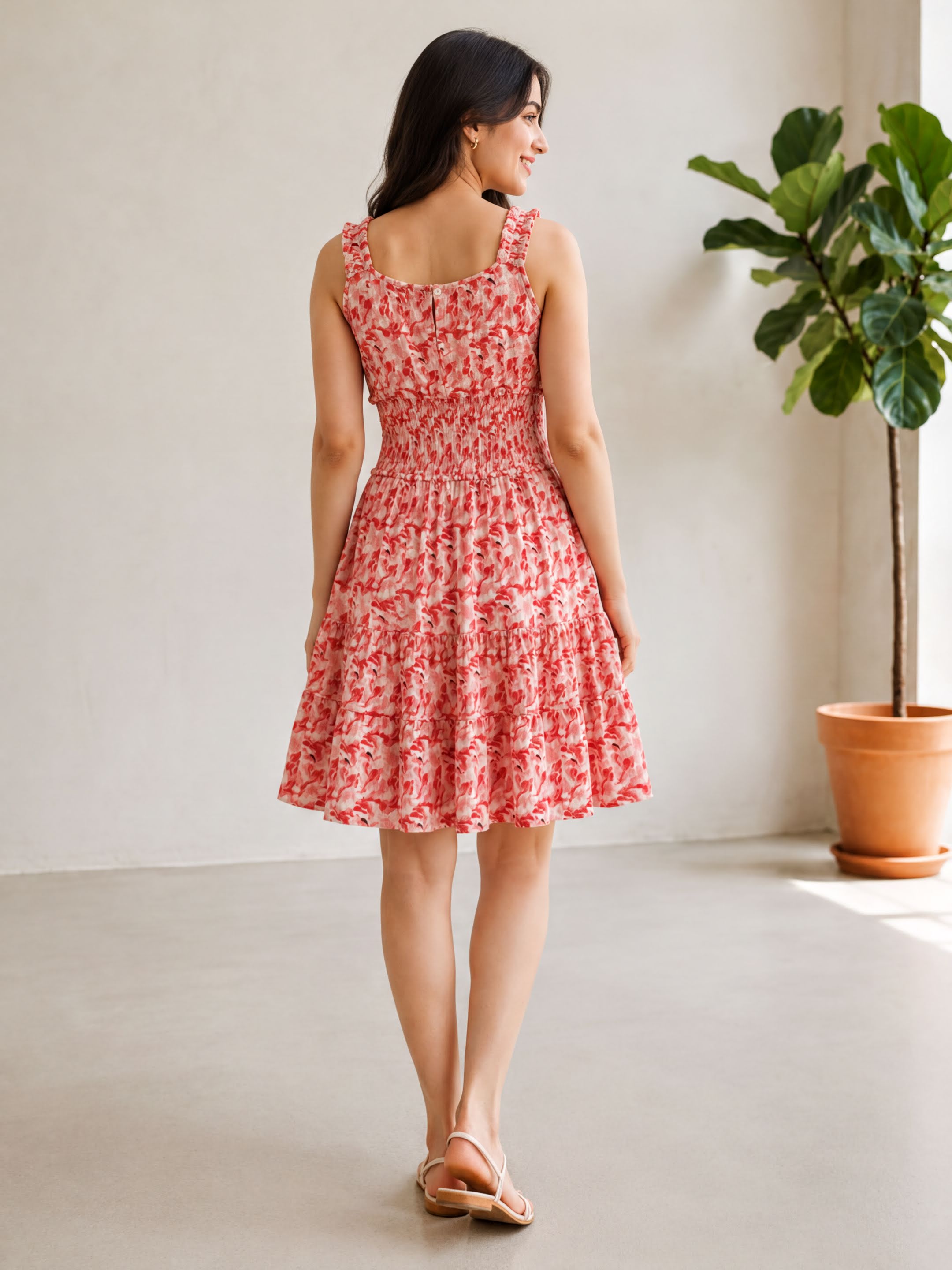A woman wearing a red and white floral dress stands in a room with a potted plant in the background.