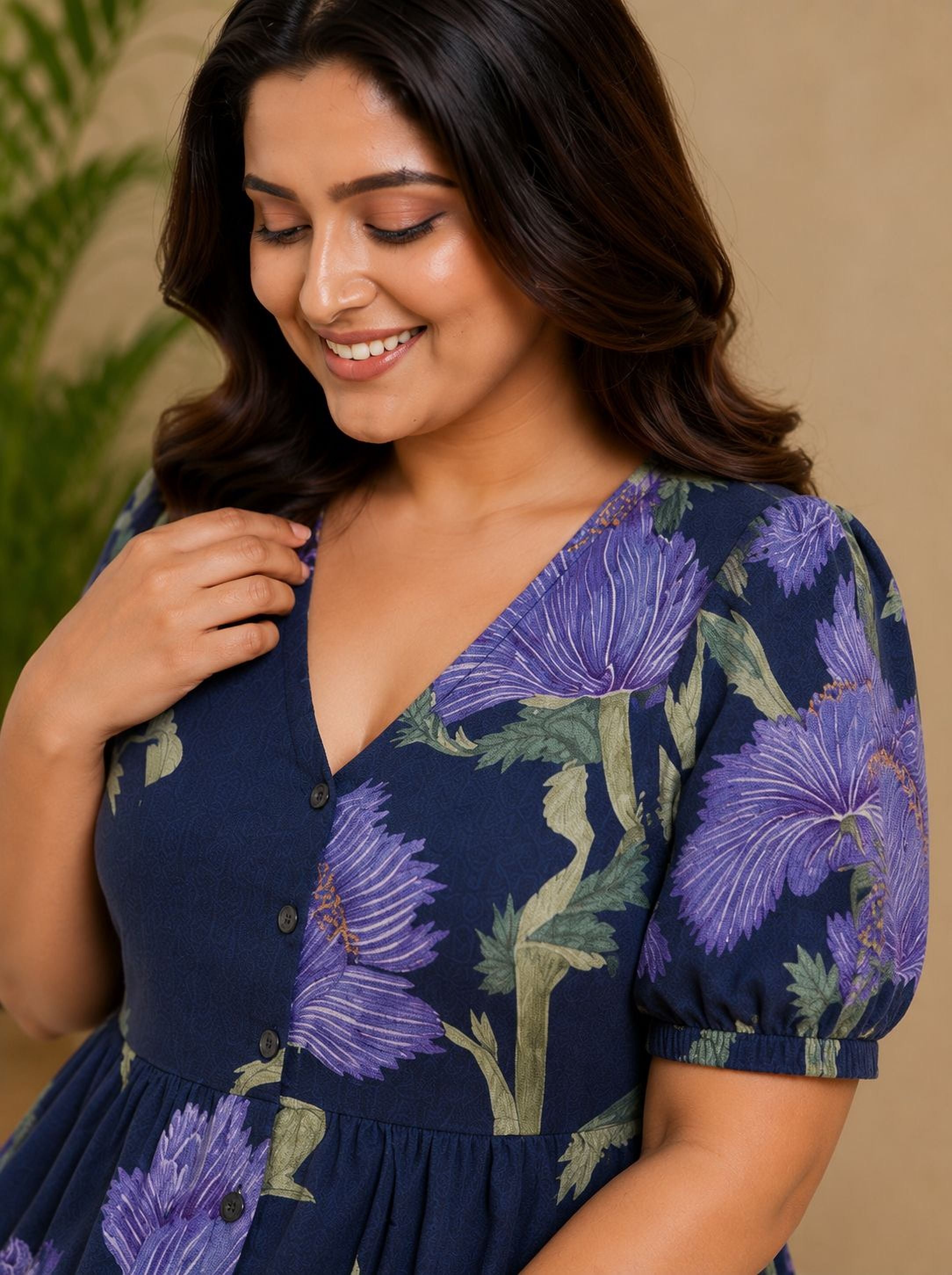 A woman with long dark hair wearing a blue dress with a floral pattern, smiling and looking down at her hand.
