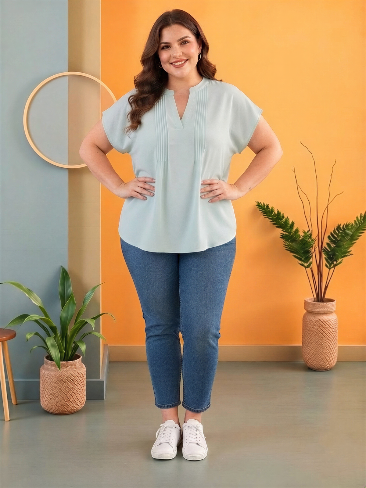 A woman wearing a light blue blouse and jeans stands confidently in a room with a vibrant orange wall, a round mirror, and potted plants.