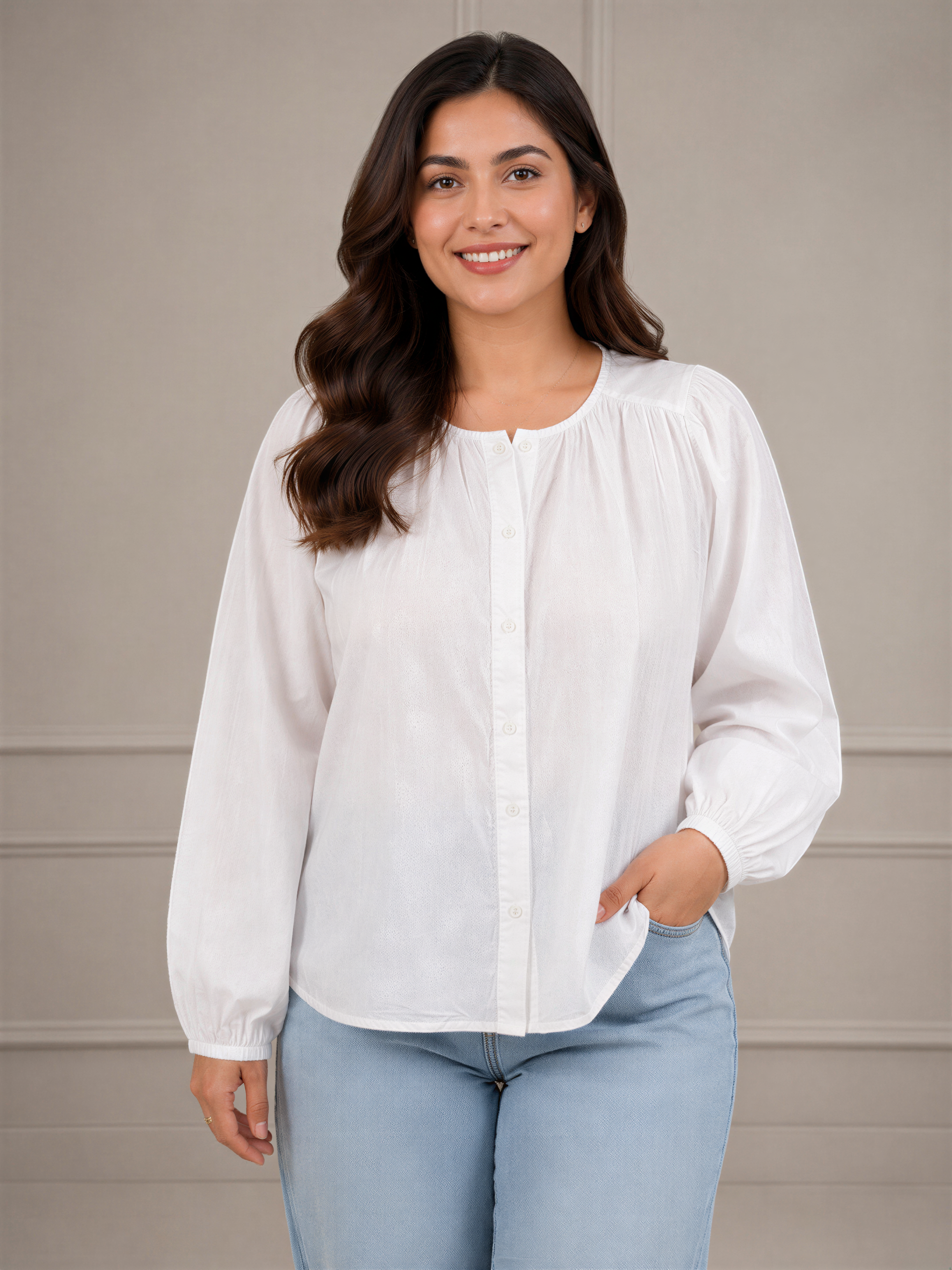 A woman with long brown hair is smiling and wearing a white blouse and light blue jeans.