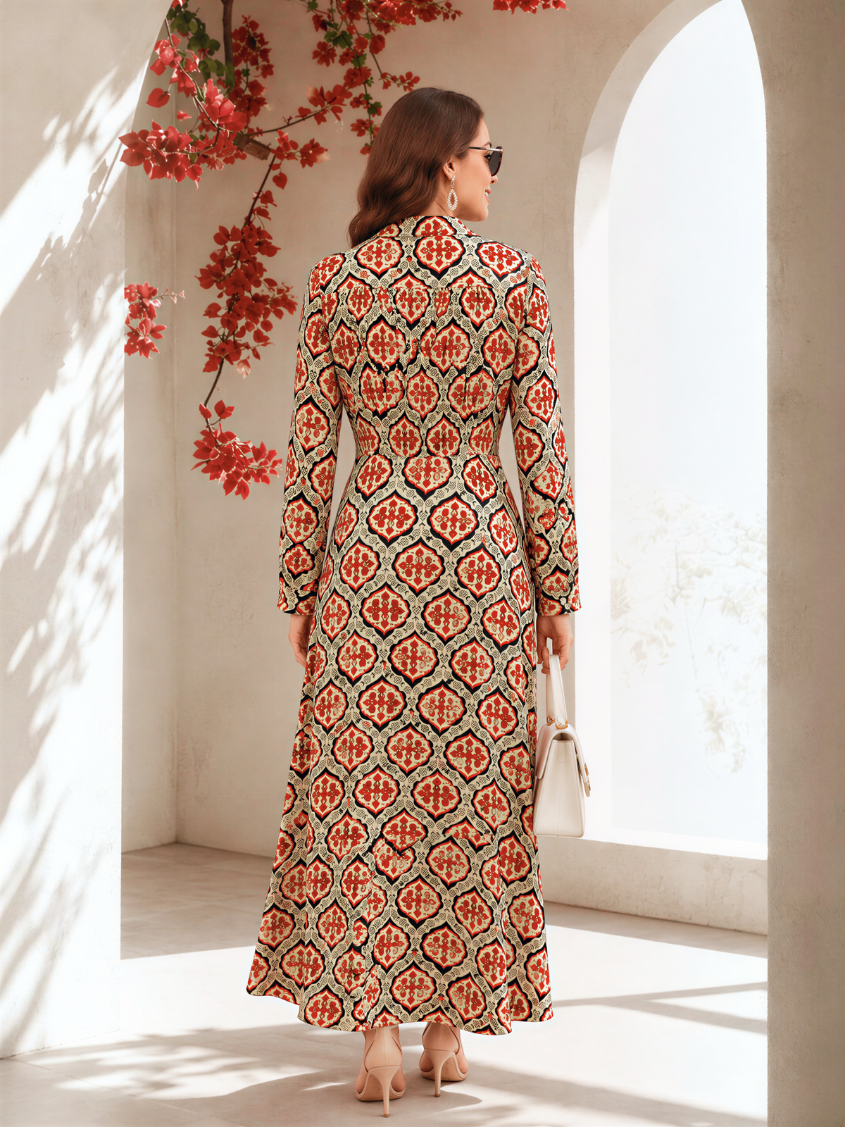A woman wearing a long, patterned dress stands in a room with arched windows and red flowers hanging from the ceiling.