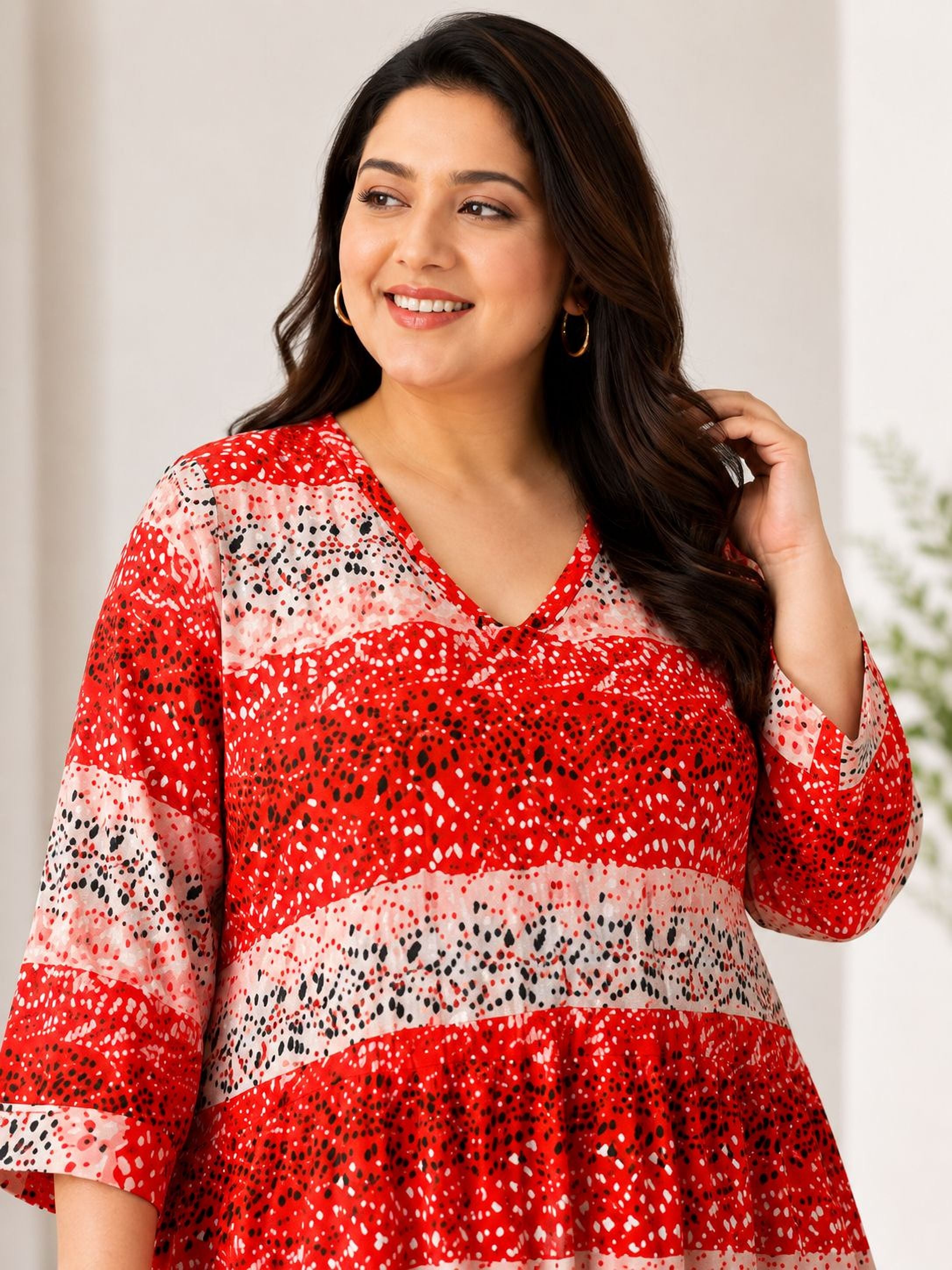 A woman with long dark hair is smiling and posing in a red and white patterned dress.